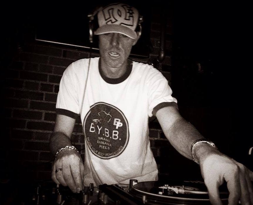 DJ Natural Nate® in black and white, BYBB circle logo tee, hands on Technics against brick wall